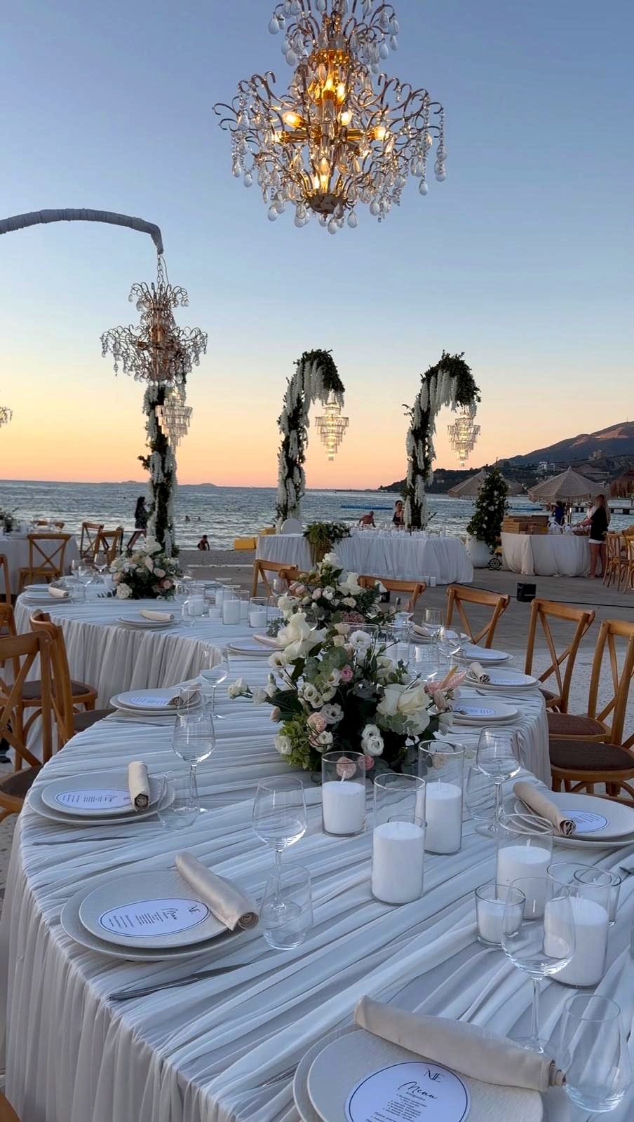 Bojo Resort Orikum — Festtafel bei Sonnenuntergang mit Kristallleuchtern und Blütenbögen am Strand