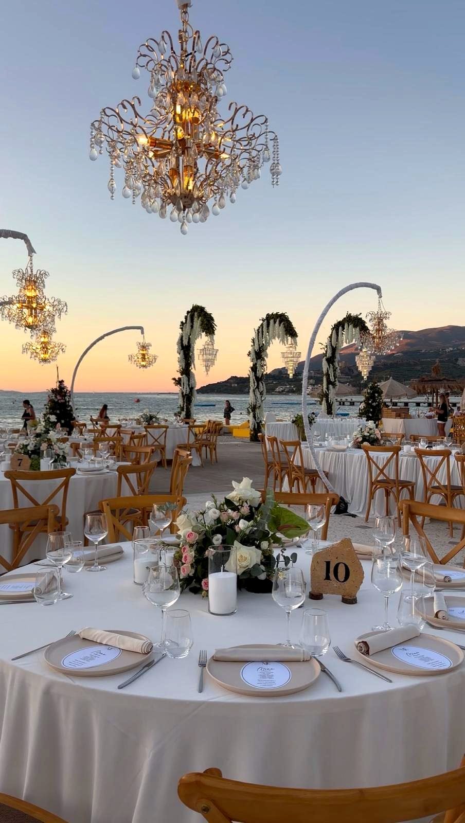 Bojo Resort Orikum — Rundtische mit Kristallleuchtern und Blütenbögen bei Sonnenuntergang